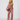 A woman modeling a dusty rose eyelet two-piece set consisting of a sleeveless V-neck top and matching wide-leg pants, styled with a dark brown crescent handbag and black sandals against a light gray studio background.