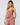 A woman modeling a dusty rose eyelet two-piece set consisting of a ruffled camisole top and matching drawstring pants against a light gray studio background.