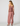 A woman shown from the back wearing a dusty rose two-piece set with a ruffled halter-style top and matching loose pants, photographed against a plain light gray studio background.