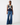 A model stands against a plain white studio background wearing a sleeveless navy satin top with cream lace trim and wide-leg blue jeans.