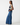A model is shown in profile wearing a sleeveless navy top with cream lace trim and wide-leg blue denim pants against a plain white studio background.