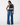 A woman shown from the back wearing a sleeveless navy top with cream lace trim and wide-leg blue jeans, photographed against a clean white studio background.