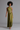 A woman modeling a sleeveless olive green halter maxi dress with a textured, patterned waist panel, photographed against a solid gray studio background.