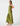 A woman modeling a sleeveless olive green maxi dress with a white polka dot pattern, shown from a side profile against a plain light gray studio background.
