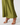 An olive green satin skirt with white polka dots, shown on a model wearing beige heeled sandals against a light gray studio background.