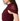 Close-up side view of a woman wearing a deep burgundy top with a sheer draped shoulder panel and side cutout, against a plain white background.