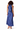 A woman shown from the back wearing a sleeveless royal blue satin halter maxi dress with a tie at the neck, paired with nude high-heeled sandals, against a plain white studio background.