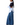 A woman shown from the side wearing a layered outfit consisting of a light blue and navy collared shirt tucked into wide-leg blue denim jeans, against a plain white background.