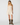 A woman modeling a cream-colored sleeveless mini dress with delicate lace detailing on the bodice and a flared skirt, paired with brown cowboy boots, against a plain light gray background.