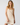 A woman modeling a cream-colored slip dress with thin spaghetti straps and a lace yoke, set against a plain light gray studio background.