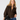 A woman modeling a brown fuzzy zip-up sweater with a faux-fur collar, paired with blue jeans and holding a black handbag with a gold chain strap, against a light gray studio background.