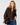 A woman modeling a brown fuzzy zip-up sweater with a faux-fur collar, paired with blue jeans and holding a black handbag with a gold chain strap, against a light gray studio background.