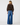 A model shown from the back wearing a dark brown knit sweater with a brown fur collar and wide-leg blue jeans, photographed against a light gray studio background.