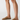 A close-up of a person's legs wearing tan suede mule loafers against a clean white studio background.