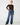 A model wearing a dark brown off-the-shoulder long-sleeve top and wide-leg blue jeans with a brown belt, standing against a light gray studio background.