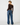 A woman is shown from the back wearing a dark brown off-the-shoulder long-sleeve crop top and wide-leg blue jeans against a plain white studio background.