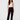 A model stands against a light gray studio background wearing dark burgundy velvet wide-leg pants, a white ribbed tank top, and black shoes.