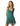 A woman modeling a sleeveless teal green dress with white polka dots and a floral print along the ruffled hem, set against a plain white background.