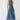 A woman modeling a sleeveless, high-neck, midi-length blue denim dress against a plain light gray studio background.