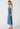 A woman modeling a sleeveless, halter-neck midi dress made of washed blue denim, shown from a side profile against a light gray studio background.