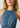 Close-up of a woman wearing a blue denim halter top with a gathered waist and decorative braided trim around the neckline.