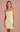Woman wearing a light yellow dress with button details on a pink background