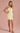 Woman wearing a light yellow dress with buttons on a pink background