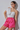 Woman wearing a white top and pink shorts against a plain background
