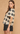 A woman wearing a short-sleeve crochet knit top with a black and cream geometric pattern, paired with black shorts, posed against a textured beige background.