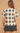 A woman shown from the back wearing a short-sleeve lace top with a black and cream geometric diamond pattern, paired with black shorts, against a textured beige background.