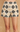 A close-up of a model wearing high-waisted crochet shorts with a black and beige geometric pattern, set against a warm beige textured background.
