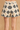 A close-up of a person wearing high-waisted crochet shorts with a black and cream geometric pattern, set against a warm beige textured background.