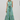 A sleeveless, multicolor vertically striped maxi dress with a tie waist and ruffled hem, modeled on a plain light gray studio background.