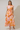 Woman wearing a floral dress with orange and pink pattern on a plain background