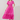 A woman modeling a bright pink midi dress with short puff sleeves, a gathered waist, and embroidered floral details, paired with white heeled sandals against a plain beige studio background.