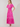 A woman modeling a bright pink midi dress with short flutter sleeves, a gathered waist, and scattered floral embroidery, standing against a plain light beige studio background.