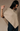 A woman wearing a beige textured knit poncho draped over her shoulders, paired with dark blue jeans, posed against a neutral beige studio background.