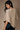 A woman wearing a beige textured knit poncho sweater, shown from the back against a neutral studio background.