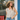 Woman wearing a floral top and straw hat standing outside a building with a blue door.
