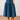 A blue tiered midi skirt with a black geometric diamond pattern, shown on a model wearing tan leather cowboy boots against a neutral indoor background.