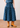 A blue tiered midi skirt with a black geometric diamond pattern, shown on a model wearing tan leather cowboy boots against a neutral indoor background.