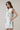 Woman wearing a white dress with colorful floral patterns on a plain background