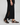 Person wearing a black dress with a slit and black sandals on a light gray background
