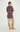 A woman stands in profile wearing a colorful striped knit sweater dress and tan suede knee-high boots against a plain light gray studio background.