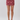 A model's lower body wearing a high-waisted, knee-length mini skirt with an intricate paisley and floral pattern in dusty rose and burgundy, paired with metallic silver high-heeled sandals against a light gray studio background.