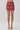 A model's lower body wearing a high-waisted, knee-length mini skirt with an intricate paisley and floral pattern in dusty rose and burgundy, paired with metallic silver high-heeled sandals against a light gray studio background.