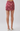 A model's lower body wearing a high-waisted, short A-line mini skirt with a pink and red paisley pattern, paired with beige block-heel mules, shot against a light gray studio background.