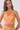 A woman modeling a peach and cream patterned two-piece set featuring a halter crop top with a large fabric flower accent at the neckline and matching high-waisted bottoms.