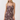 A woman modeling a sleeveless mini dress with a brown and beige botanical print and pink button accents, photographed against a plain light gray studio background.