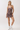 A woman modeling a brown and beige patterned mini dress with pink buttons, paired with white socks and white sneakers, against a plain white studio background.